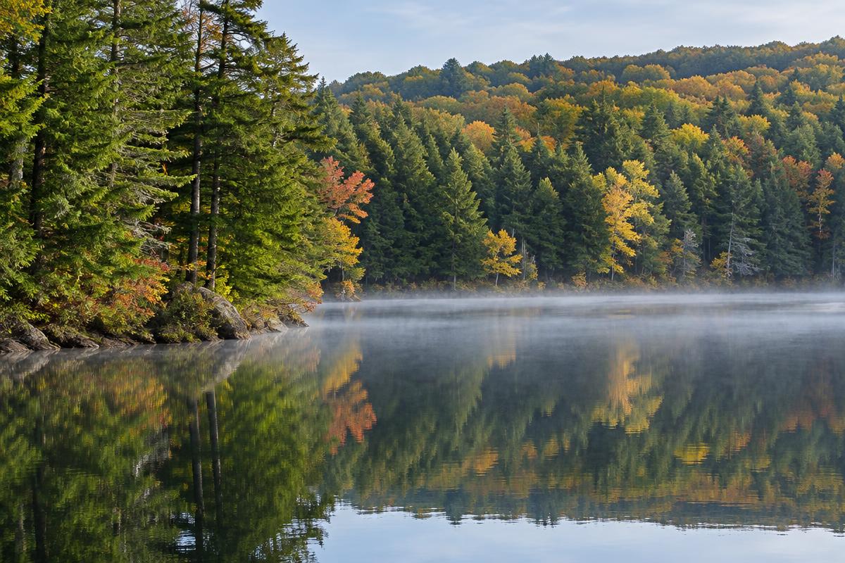 Still northern Pocono lake reflecting hemlock and autumn hardwoods with thin morning mist along the shoreline